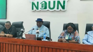 Panel of five people seated at a conference table with microphones; a man in a blue shirt and hat speaks, NDUN branding visible behind them.