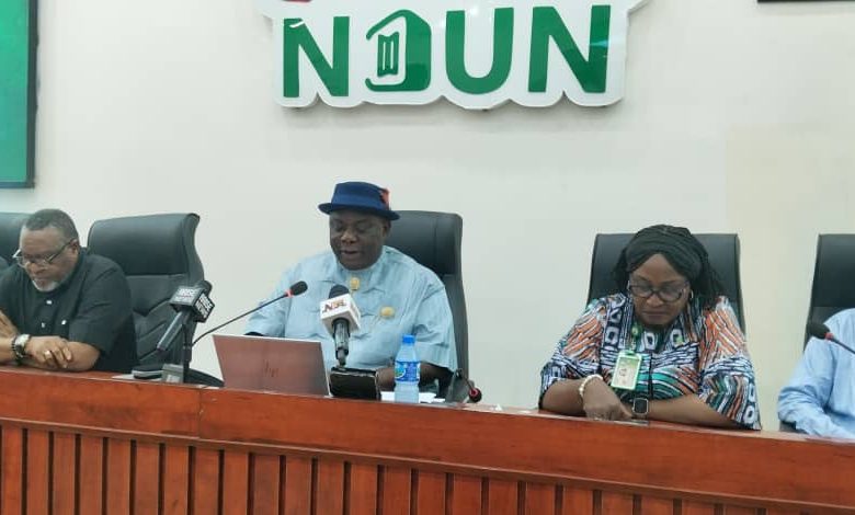 Panel of five people seated at a conference table with microphones; a man in a blue shirt and hat speaks, NDUN branding visible behind them.