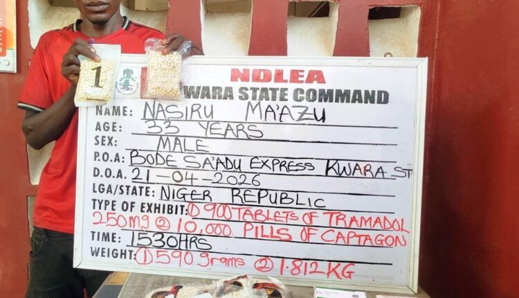 Man in a red shirt stands beside a white information board from NDLEA Warra State Command, showing detainee details (name Nasiru Mazu, age 33, male) and a drug seizure note.