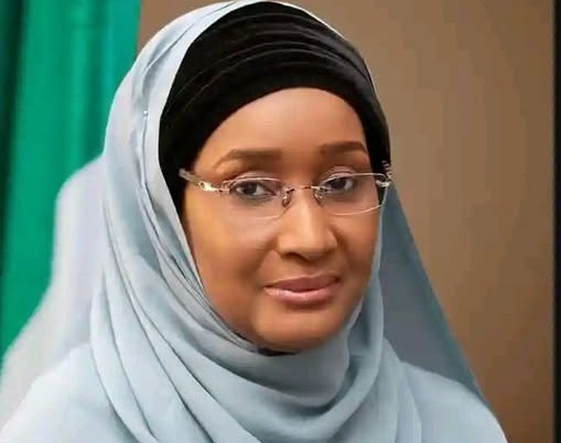 Portrait of a woman wearing a light blue hijab and glasses, looking at the camera with a gentle smile.