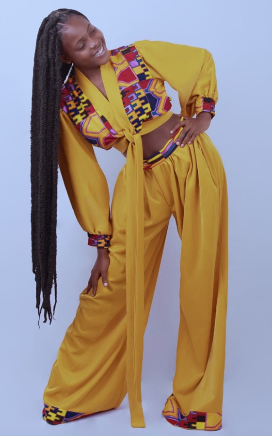 Woman wearing a mustard yellow two-piece outfit with colorful patterned accents, posing with hand on hip and smiling.
