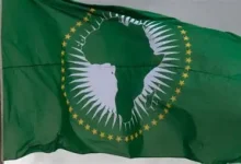 Green flag waving, featuring a white silhouette of Africa inside a ring of gold stars (African Union flag).