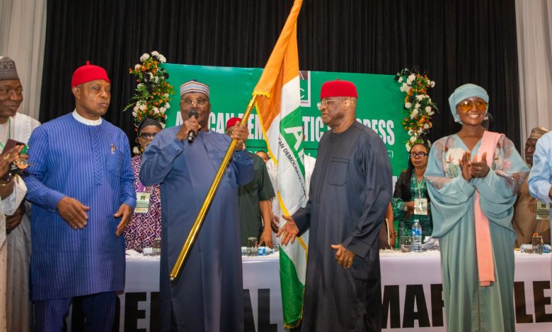 Atiku wins 1 - The Times of Abuja Group of people in colorful traditional Nigerian attire on a stage, a man holds a Nigerian flag while others applaud or speak.