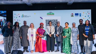IMG-20260520-WA0001 - The Times of Abuja Group of diverse professionals posing on a conference stage, in front of a banner with logos and a large QR code.