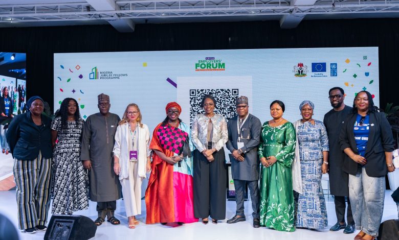 IMG-20260520-WA0001 - The Times of Abuja Group of diverse professionals posing on a conference stage, in front of a banner with logos and a large QR code.