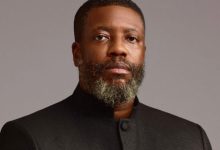 Portrait of a Black man with a gray beard wearing a black mandarin-collar jacket, looking at the camera.