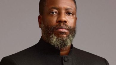 Portrait of a Black man with a gray beard wearing a black mandarin-collar jacket, looking at the camera.