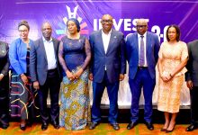 Eight professionals in formal wear posing on a stage with a purple 'INVEST 2.0' banner behind them.