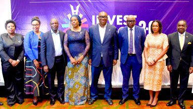 Eight professionals in formal wear posing on a stage with a purple 'INVEST 2.0' banner behind them.
