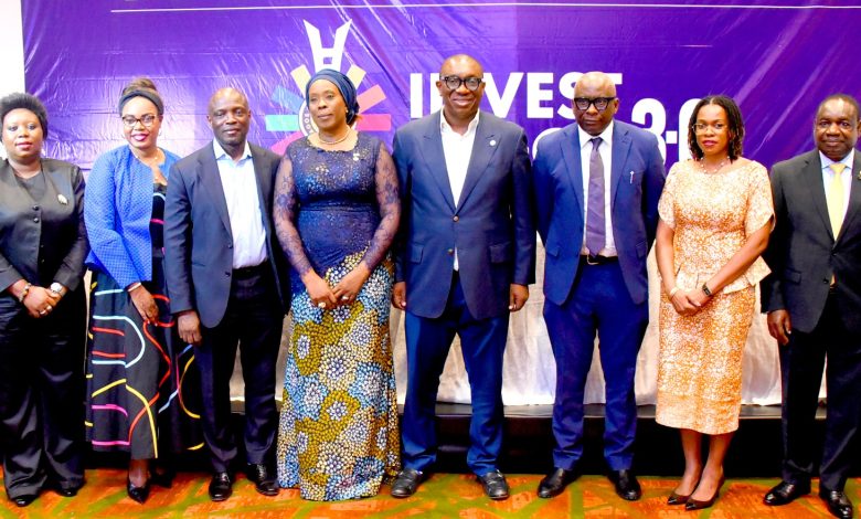 Eight professionals in formal wear posing on a stage with a purple 'INVEST 2.0' banner behind them.