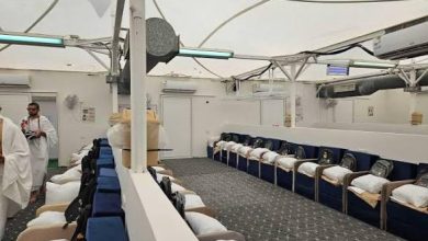 Interior of a transport vessel lounge with blue-cushioned seats along the walls and crew members in white in the background.