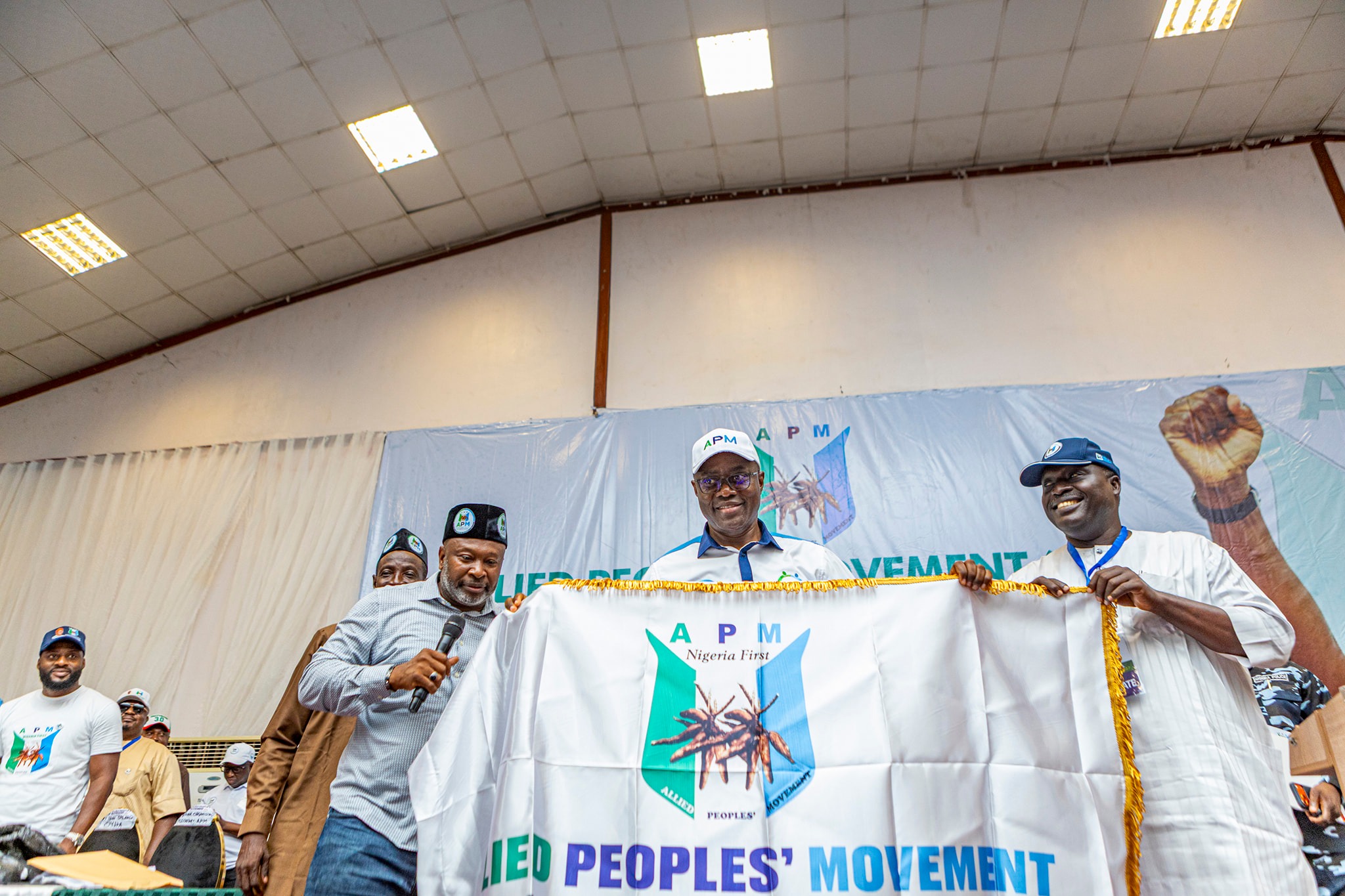 Seyi Makinde 2 - The Times of Abuja Group of men on stage holding a banner for a Nigerian political movement at an indoor event.