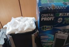 Box for a JBL CristalProfi aquarium filter beside a black canister filter with a white bag on top, on a shelf.