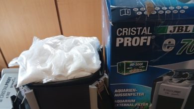 Box for a JBL CristalProfi aquarium filter beside a black canister filter with a white bag on top, on a shelf.
