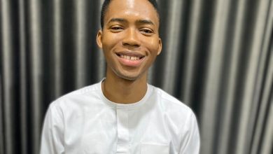 Smiling man in a white shirt standing in front of dark striped curtains.