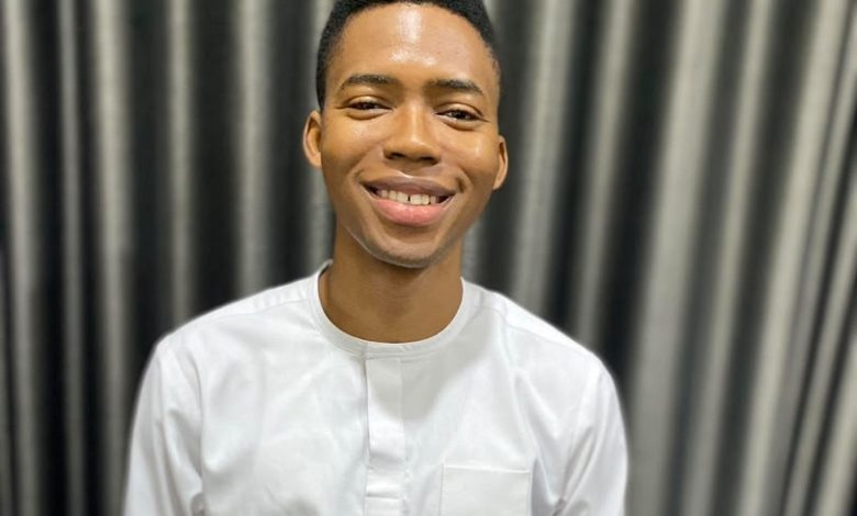 Smiling man in a white shirt standing in front of dark striped curtains.