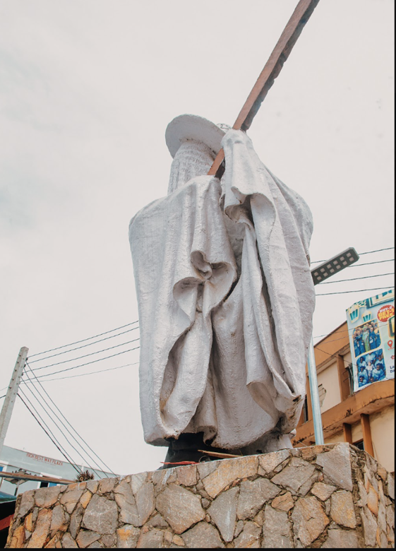Statue wrapped in white cloth mounted on a stone pedestal in an outdoor urban setting.