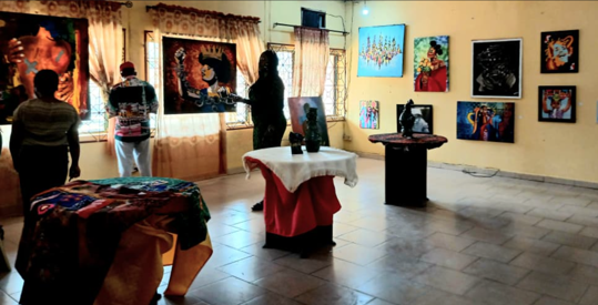 FEAAN International Womens Day Exhibition 1 - The Times of Abuja People viewing colorful paintings in a bright gallery with framed artworks on yellow walls, several attendees examining the pieces from a distance.