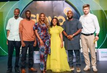 Six diverse adults posing for a group photo on a stage, with neon Glovo Summit signage behind them.