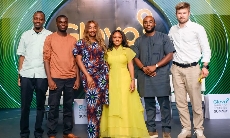 Six diverse adults posing for a group photo on a stage, with neon Glovo Summit signage behind them.