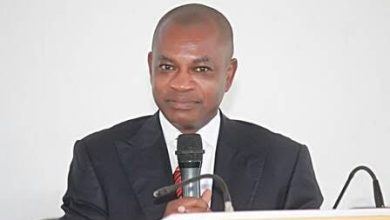 Man in a dark suit delivering a speech at a podium, holding a handheld microphone