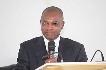 Man in a dark suit delivering a speech at a podium, holding a handheld microphone