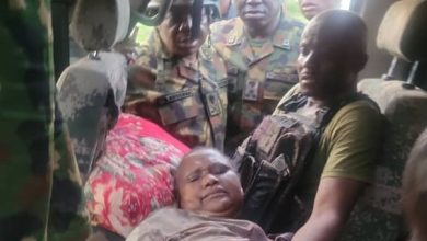Late Abubakars wife - The Times of Abuja Woman lying on a car seat as soldiers surround her and assist, with a man supporting her on the right.