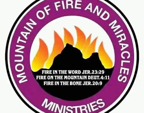 Moutain of Fire - The Times of Abuja Logo for Mountain of Fire and Miracles Ministries: a purple circular emblem with white edge text around a black mountain and orange flames, featuring Bible verses Jeremiah 23:29; Deuteronomy 4:11; Jeremiah 20:9 in the center.