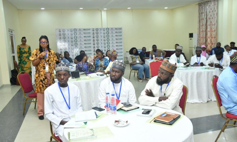 State monitoring officers - The Times of Abuja Group of people in a conference room seated at round tables, one woman standing and speaking into a microphone; banners and notebooks on tables suggest a formal workshop.