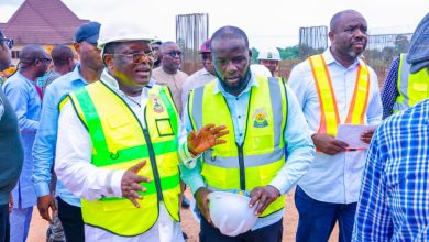 Group of construction workers and officials in high-visibility vests discussing at a site, one man holding a hard hat.
