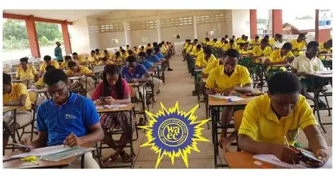 WAEC candidates - The Times of Abuja Students in yellow uniforms sit at desks taking an exam in a large classroom; a WAEC logo is visible in the center foreground.