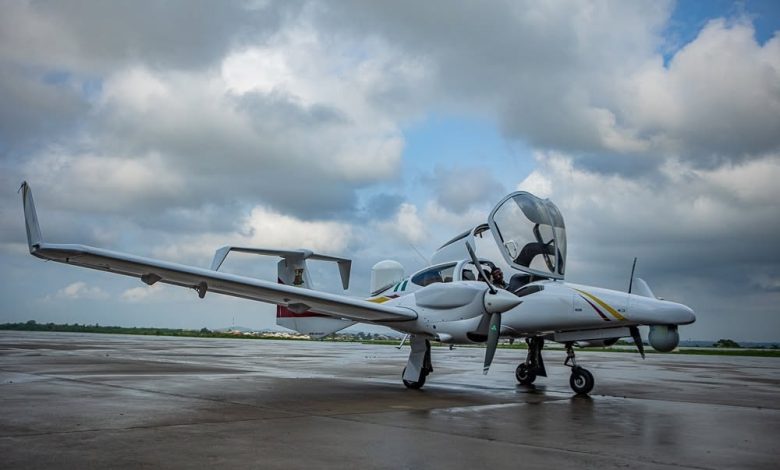Small white twin-engine plane on a wet tarmac with open cockpit canopy and overcast sky in the background.