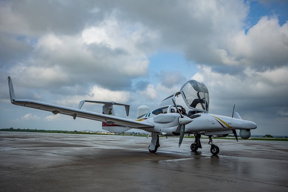 Small white twin-engine plane on a wet tarmac with open cockpit canopy and overcast sky in the background.