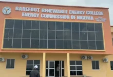 Front view of Barefoot Renewable Energy College building with an orange facade and a large sign reading 'Barefoot Renewable Energy College – Energy Commission of Nigeria' above the glass facade.