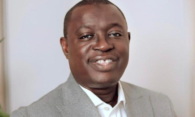 Portrait of a smiling man wearing a light gray blazer and white shirt, facing the camera.