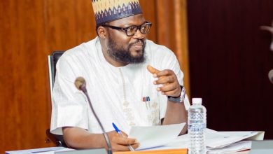 David Daser president and chief executive officer of DBI - The Times of Abuja Man in traditional attire and patterned cap sitting at a desk with papers, speaking and gesturing during a meeting.