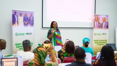 Presenter in a colorful outfit speaks to an audience at the front of a conference room with banners on both sides for the NHEF University Advancement Program, and a projected slide above her.