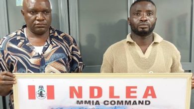 Two men stand indoors, each holding a framed NDLEA MMIA Command board with handwritten details.