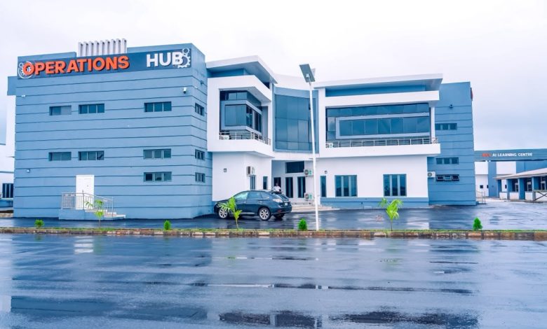 Imo Digital city 1 - The Times of Abuja Blue modern office building labeled 'OPERATIONS HUB' with a parked car in front on a wet road, overcast sky nearby.