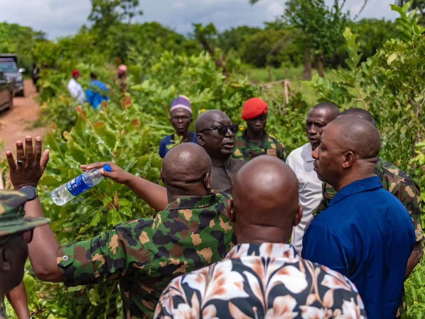 Inspection of Kwara battalion camp site 1 - The Times of Abuja Group of men, some in camouflage, gathered in a lush outdoor garden, with a water bottle being offered.