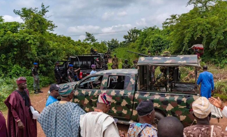 Inspection of Kwara battalion camp site 2 - The Times of Abuja Military personnel in camouflage with armed trucks on a dirt rural road, as civilians gather nearby.
