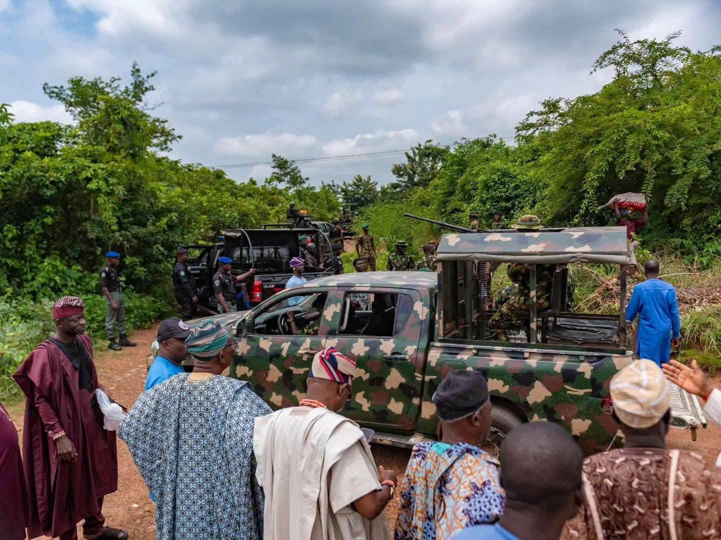Inspection of Kwara battalion camp site 2 - The Times of Abuja Military personnel in camouflage with armed trucks on a dirt rural road, as civilians gather nearby.