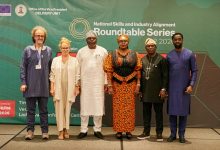 Six diverse professionals posing for a photo in front of a green conference backdrop that reads 'National Skills and Industry Alignment Roundtable Series.'