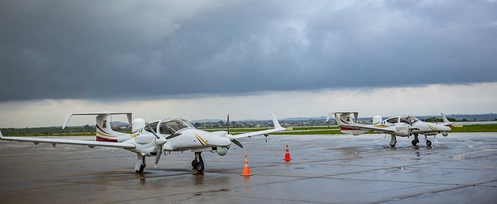 Two small white propeller planes parked on a wet tarmac beneath a dark cloudy sky, with orange cones nearby.
