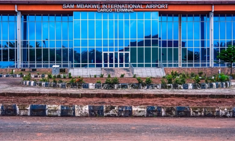 Sam Mbakwe airport - The Times of Abuja Front view of Sam Mbakwe International Airport Cargo Terminal with glass facade and a circular landscaped curb in the foreground, under a blue sky.