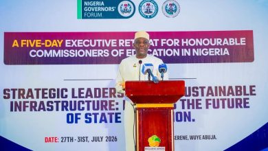 Man in white traditional attire speaks at a podium during a Nigeria Governors' Forum event, with a large banner behind him.