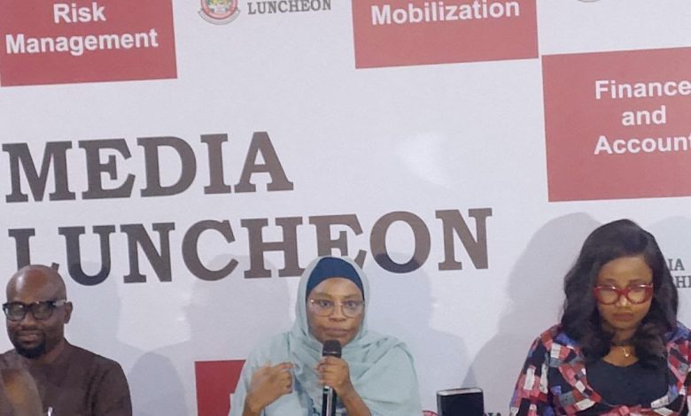 UBEC launcheon - The Times of Abuja Woman in a light blue hijab speaks into a microphone at a media luncheon panel, with a 'Media Luncheon' backdrop.