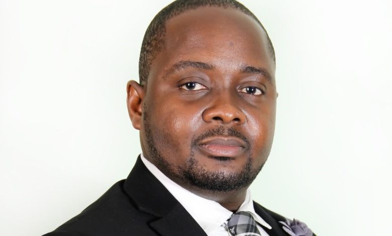 Wusu Rotimi - The Times of Abuja Professional headshot of a man in a dark suit and plaid gray tie, facing the camera with a neutral expression.