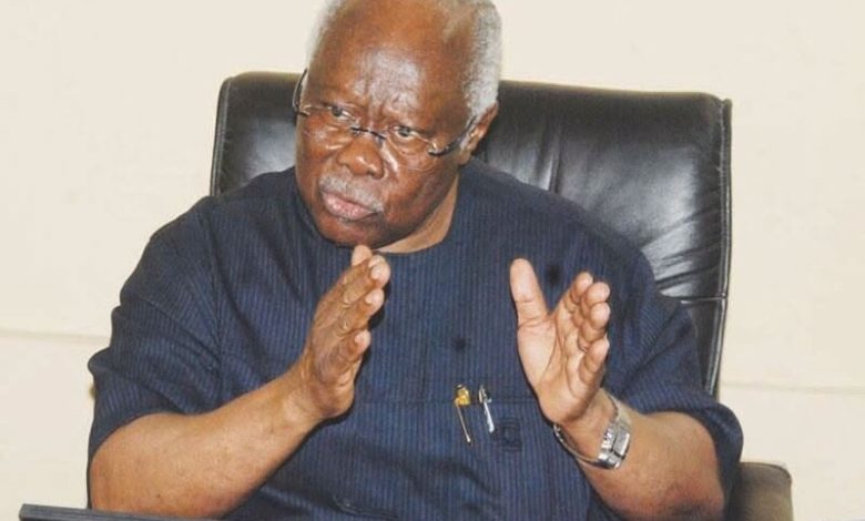 Bode George - The Times of Abuja Older man with glasses in a dark blue shirt sits in a leather chair, gesturing with his hands while talking.