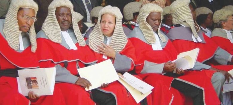 Judges - The Times of Abuja Group of judges wearing red robes and white wigs seated with documents at a formal ceremony.
